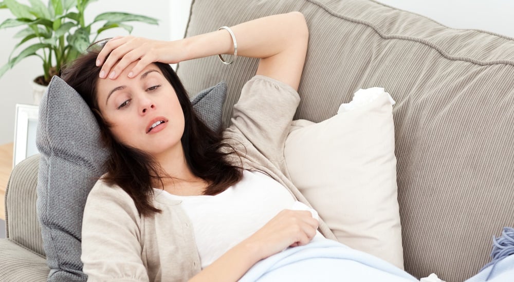 Indisposed woman feeling her temperature while resting on the sofa at home